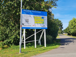 Großes Schild auf weißen Stelzen mit der Schrift "Baugebiet Klostermoor"