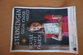 Frau hält ein Plakat mit der Aufschrift 'STERN SINGEN GEGEN KINDER ARBEIT SCHULE STATT FABRIK'