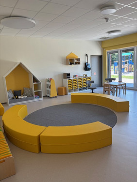 Gruppenraum mit gelbem, rundem Sofa und großen Fenstern