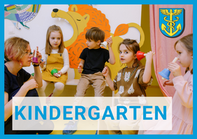 Gruppe von Kindern und Erwachsenen in einem Kindergartenraum mit bunten Wandbildern