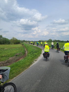 Gruppe von Radfahrern mit gelben Warnwesten auf einem Landweg unter bewölktem Himmel
