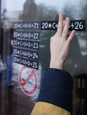 Hand zeigt mit zwei Fingern auf eine Glasfläche mit mehreren handschriftlichen Zahlen