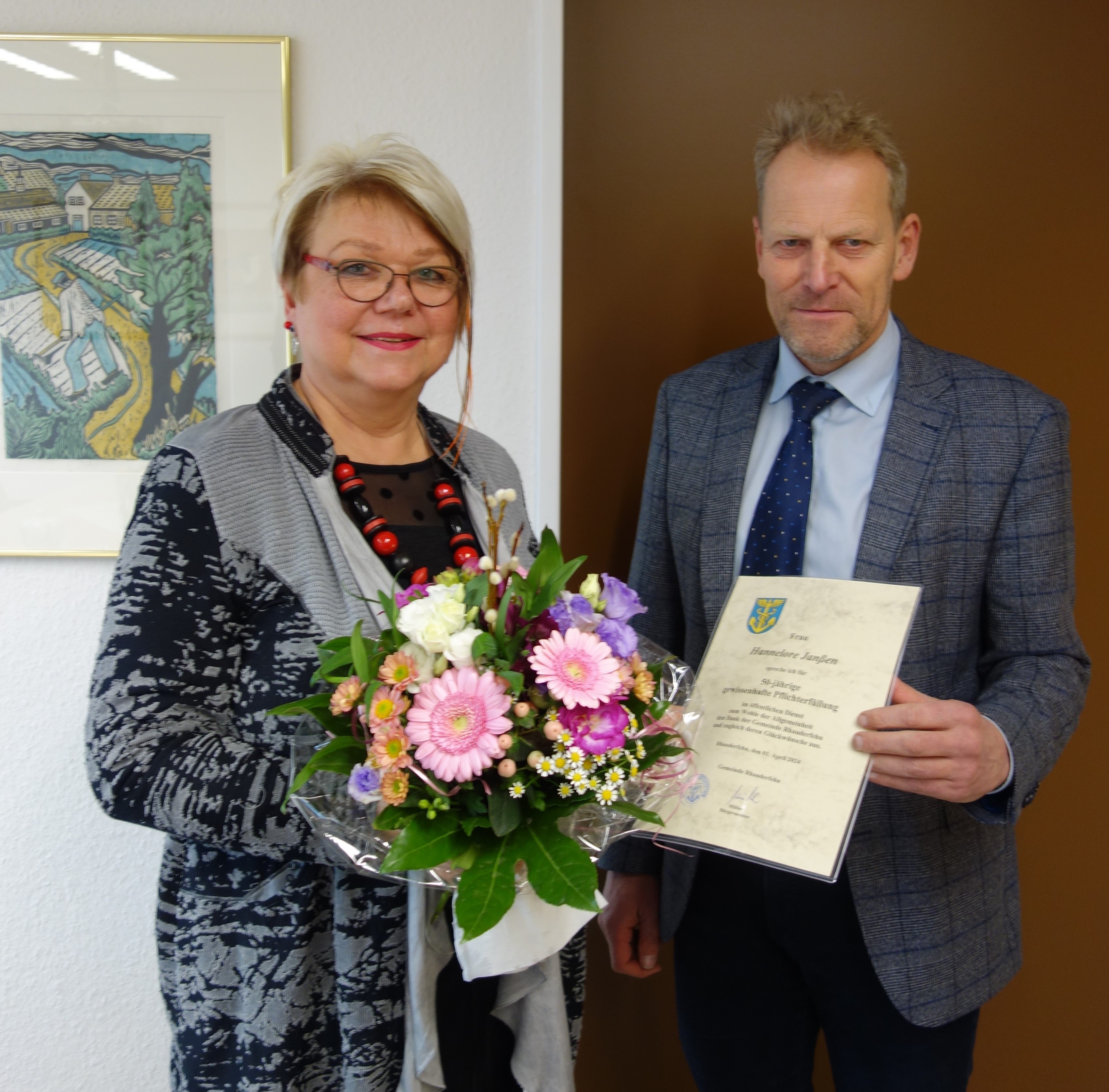 Zwei Personen stehen nebeneinander, eine hält einen Blumenstrauß, die andere eine Urkunde